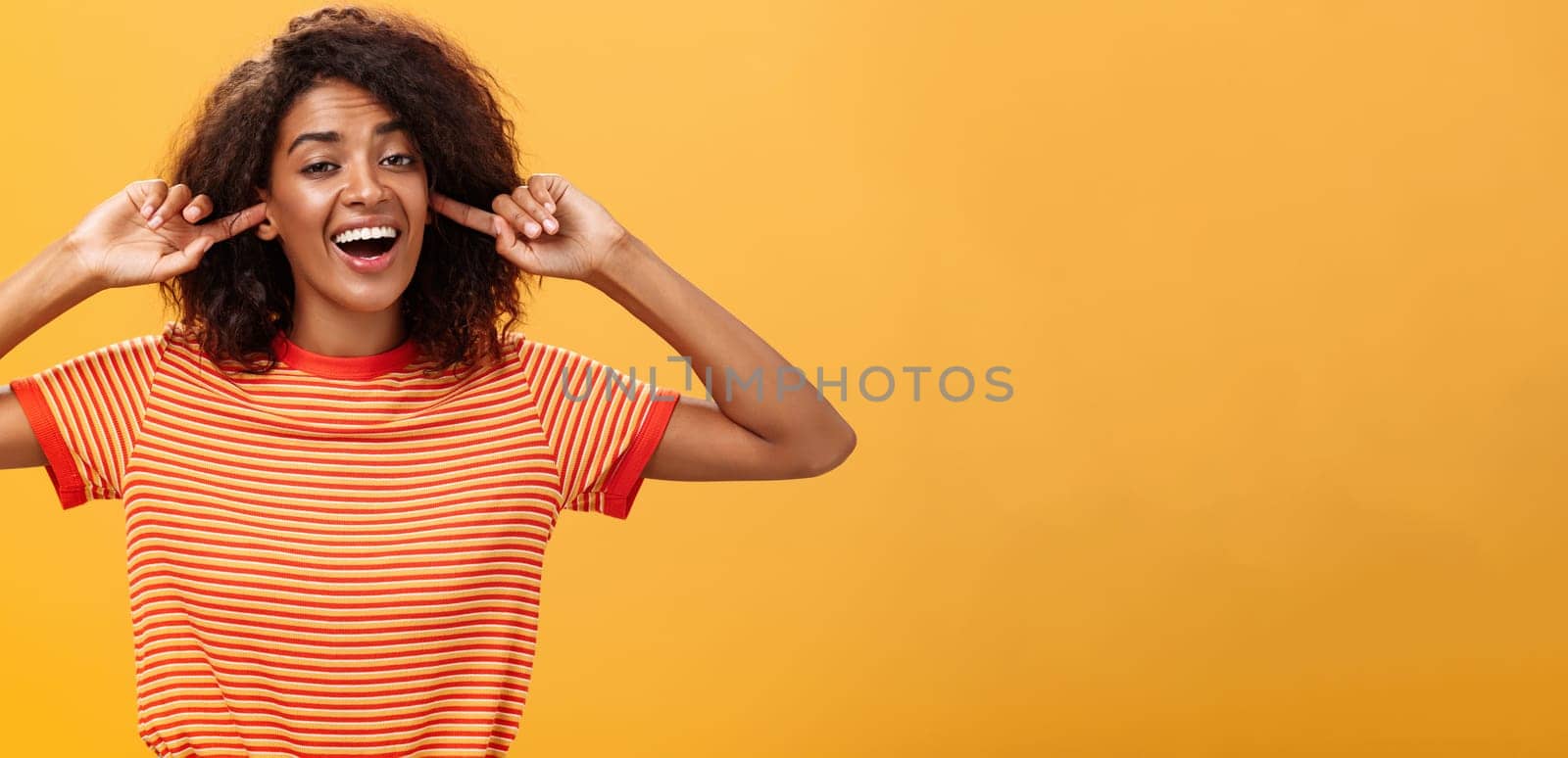 Do not care what saying cannot hear you. Carefree indifferent good-looking african american woman with curly hairstyle closing ears with index finger singing lalala during argument behaving childish.