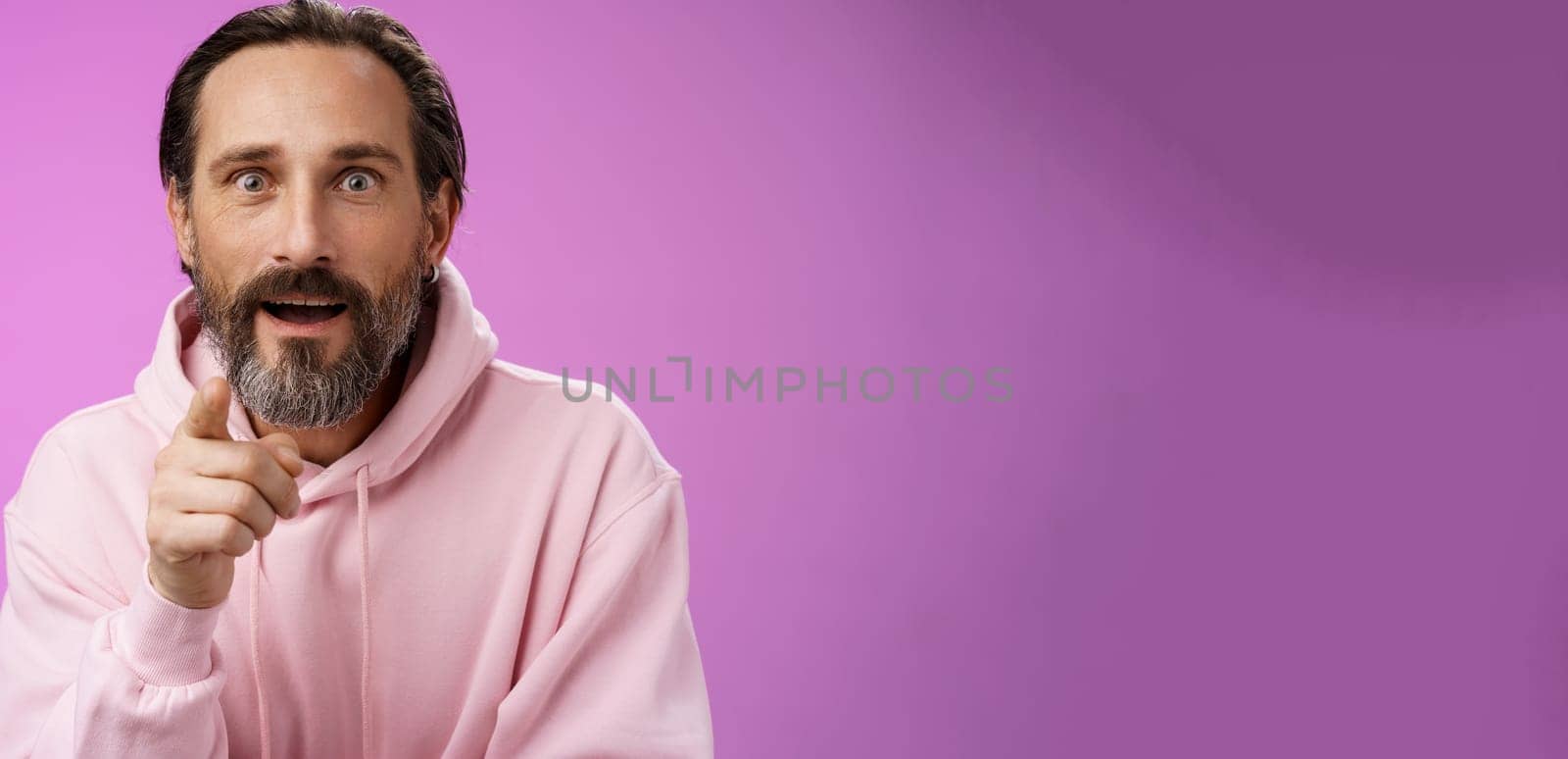 Fascinated amused european bearded mature guy widen eyes shocked open mouth recognize person pointing camera index finger surprised see familiar famous star, standing purple background.