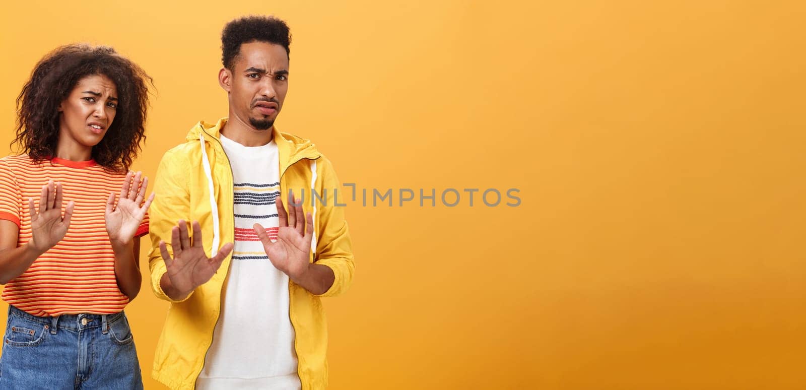 Two african american stylish friends hanging around interrupted by weird guy offering strange proposal shaking hands near chest in refusal and rejection gesture grimacing from aversion and dislike. People and emotions concept