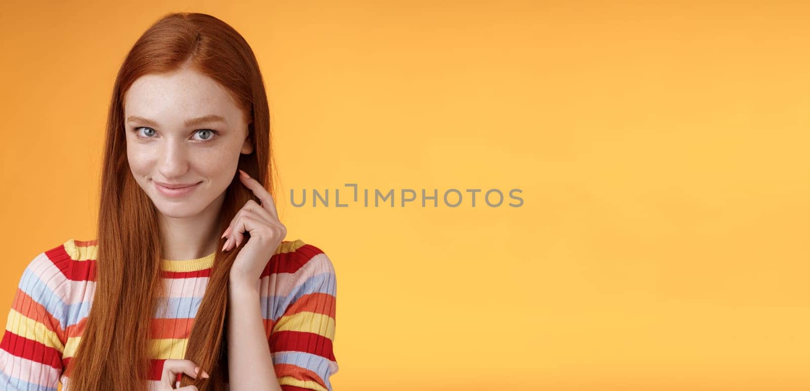 Romantic flirty shy attractive redhead girl 20s touching hair strand smiling silly modest glancing camera coquettish making lovely glances wanna seduce guy expressing sympathy, orange background by Benzoix
