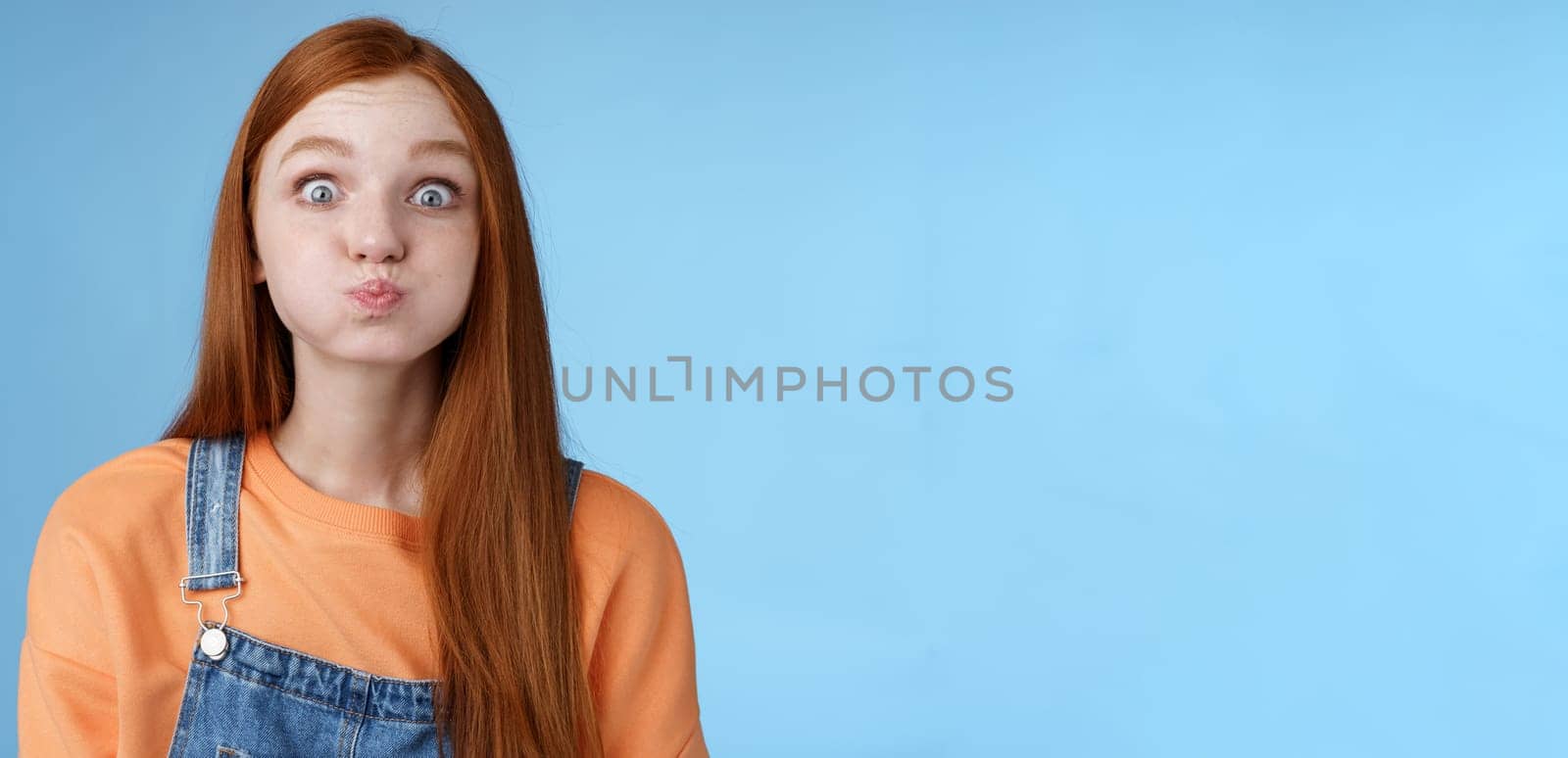 Lifestyle. Cute childish playful charming redhead girl popping blue eyes staring camera hold breath inhale air mouth standing speechless promise not slip secret acting immature standing funny happily.