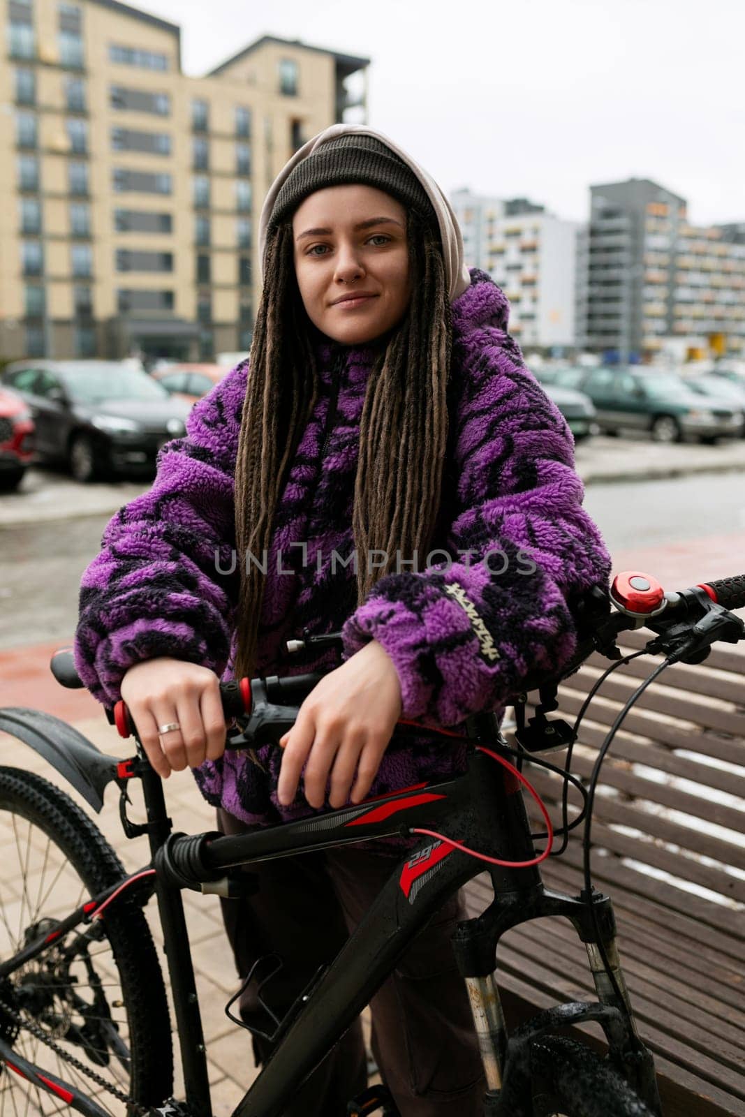 Healthy lifestyle concept. A woman with dreadlocks and piercings is waiting for friends under the entrance with a bicycle.