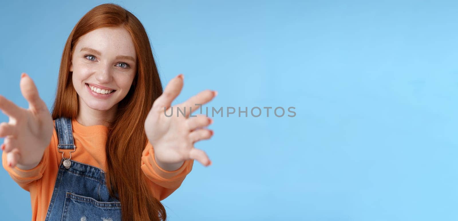 Come into arms. Charming sincere happy kind redhead girl baby sitting stretch hands camera wanna hold catch smiling friendly asking pass object, standing blue background reach friend give cuddles.