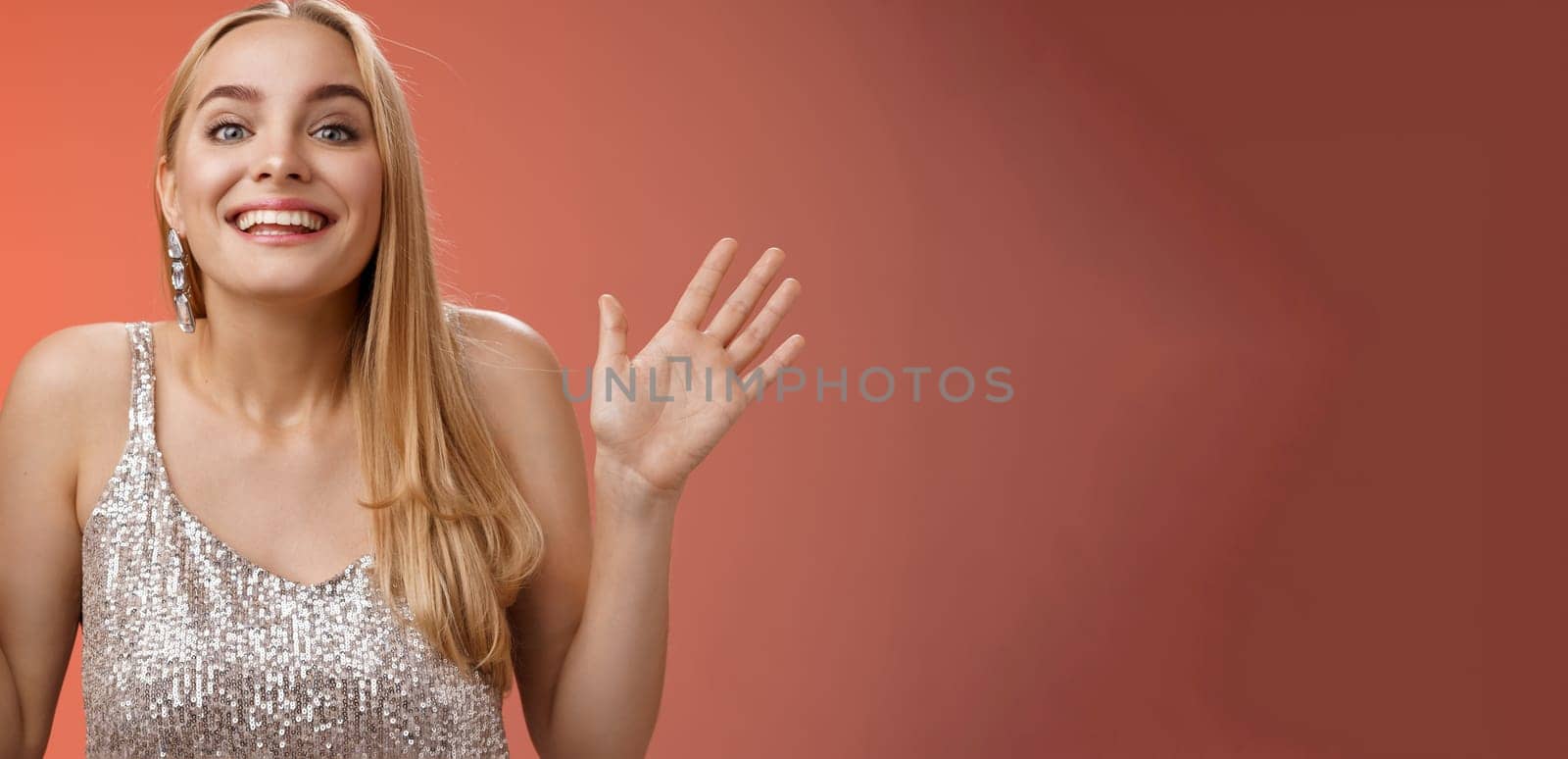 Happy elegant dreamy glamour young blond woman raising hands delight joyfully smiling camera glad see friends comming party welcoming guests grinning happily, wearing silver stylish dress.