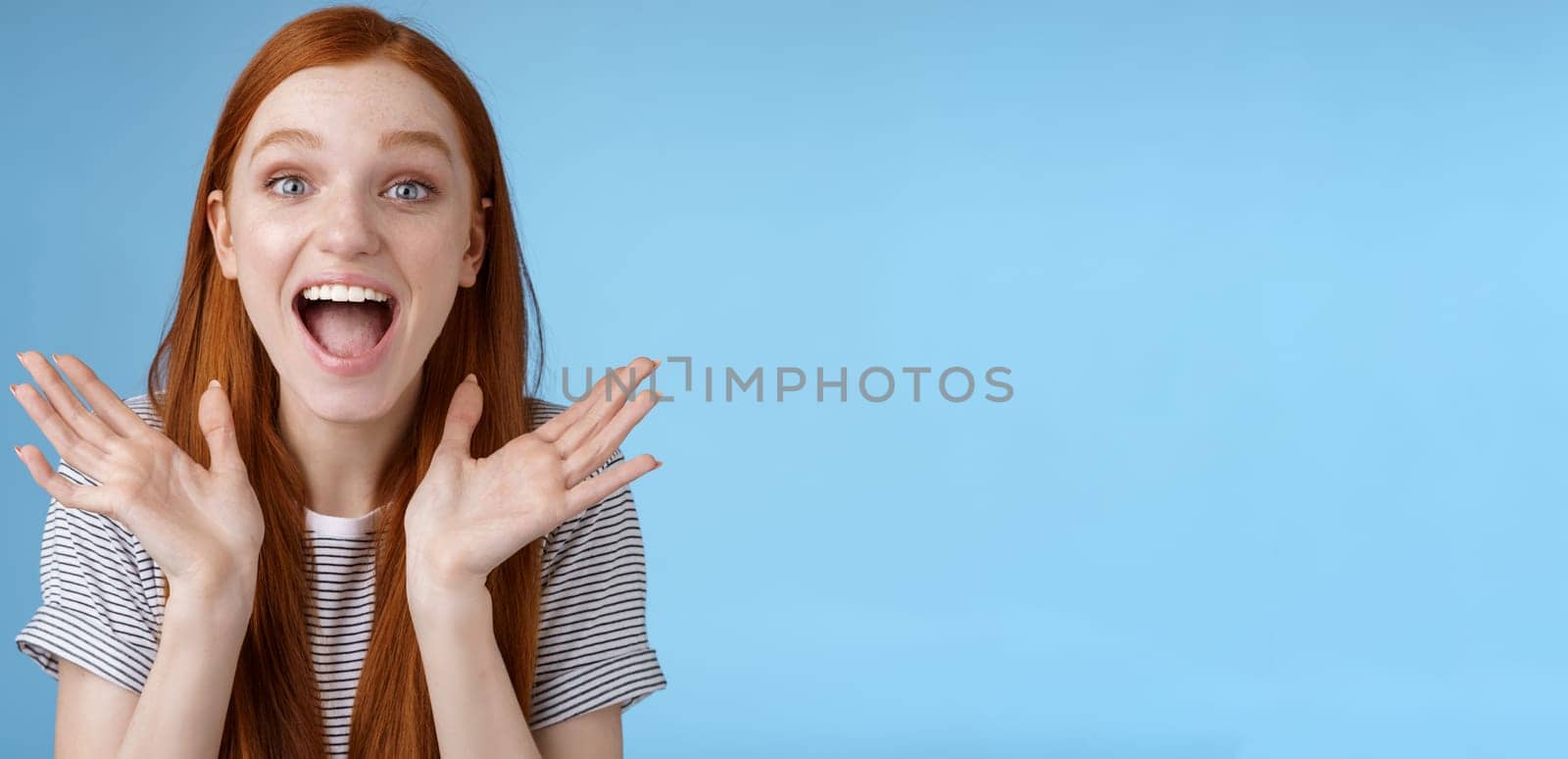 Happy cheerful rejoicing young pretty redhead supportive girlfriend clasp hands joyfully yelling congratulations raising hands amused wide eyes surprised getting awesome good news, blue background.