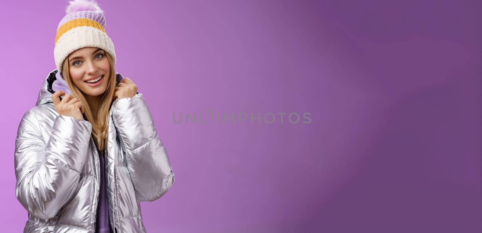 Tender feminine gentle blond girlfriend posing boyfriend take pictures ski resort holiday wearing glittering stylish jacket winter hat standing pleased purple background smiling delighted by Benzoix