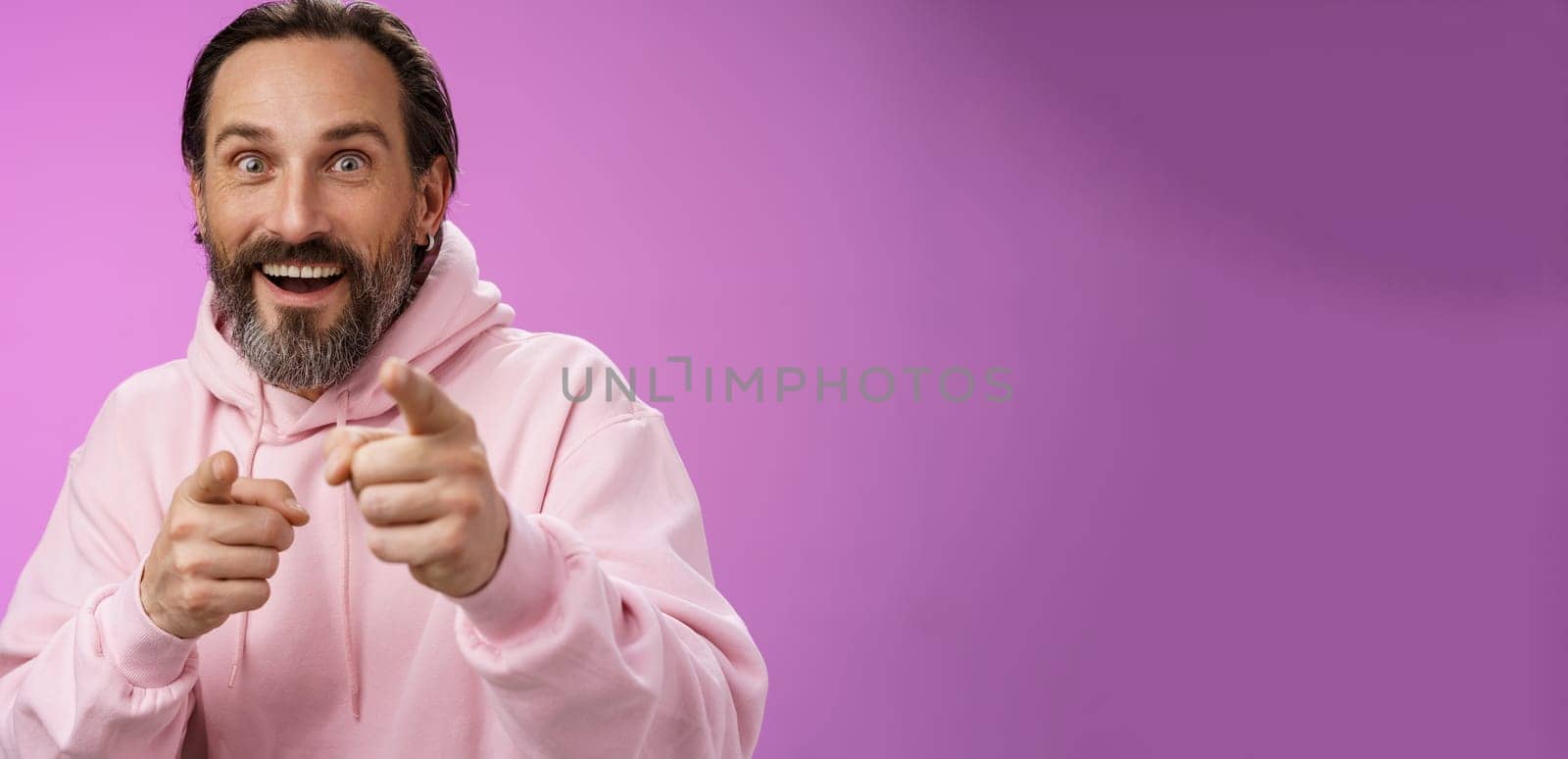 Thrilled energized charismatic happy lucky adult handsome bearded man pointing camera smiling widen eyes gazing impressed see famous person express amazement joy, purple background.
