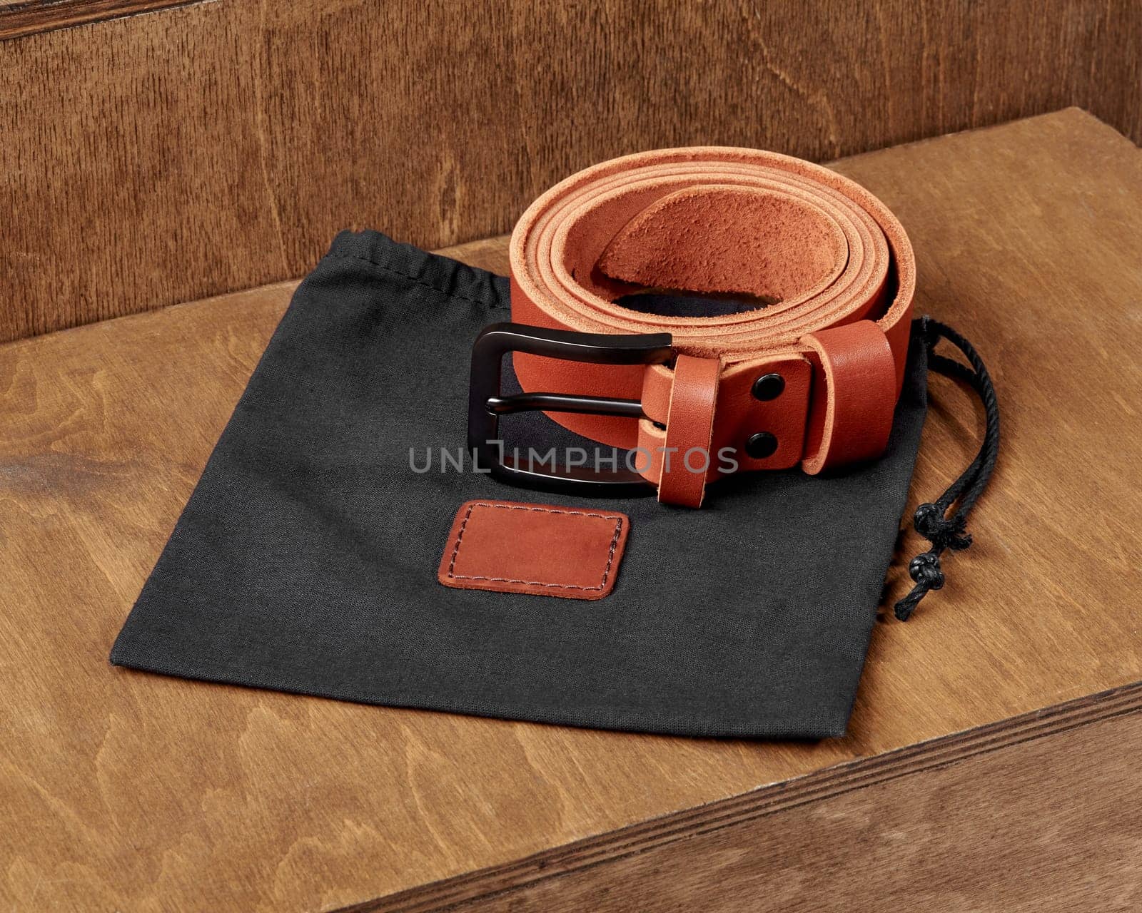 Custom copper-colored leather belt with DAD embossed on loop, accompanied by black fabric drawstring pouch, displayed on rustic wooden stand. Stylish personalized handcrafted accessory