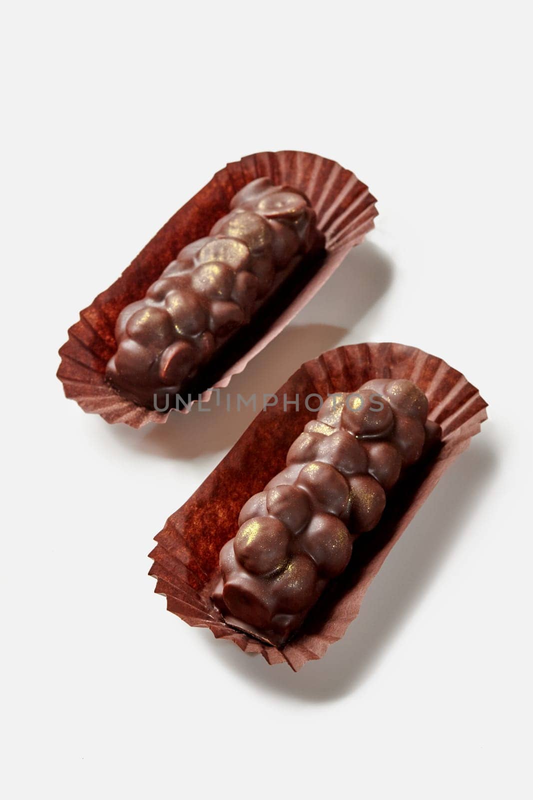 Two artisan dark chocolate bars with hazelnuts in brown paper wrappers presented on white surface, showcasing luxury confectionery