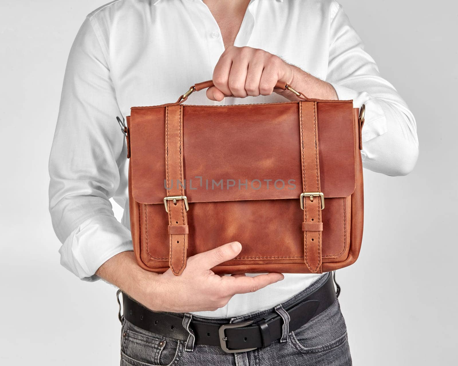 Man in white shirt and jeans showcasing custom-tailored brown leather briefcase, embossed with initials JEN, suitable for professional settings. Stylish mens accessory