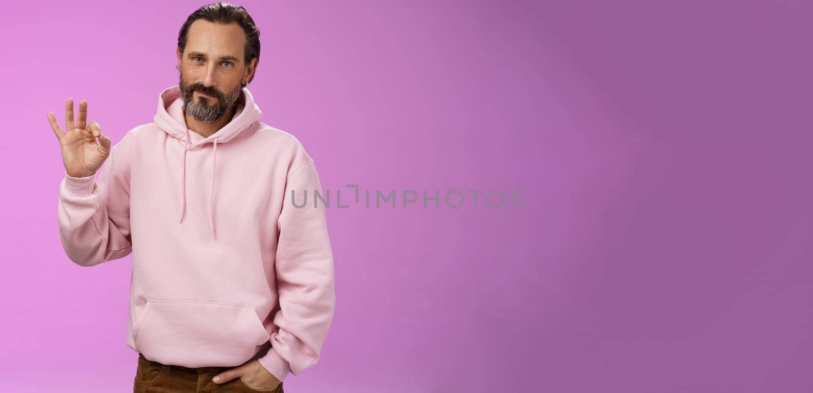 Confident good-looking lucky old macho guy bearded grey hair in stylish pink hoodie hold hand pocket show okay ok approval gesture smirking delighted agree daughter choice, posing supportive.