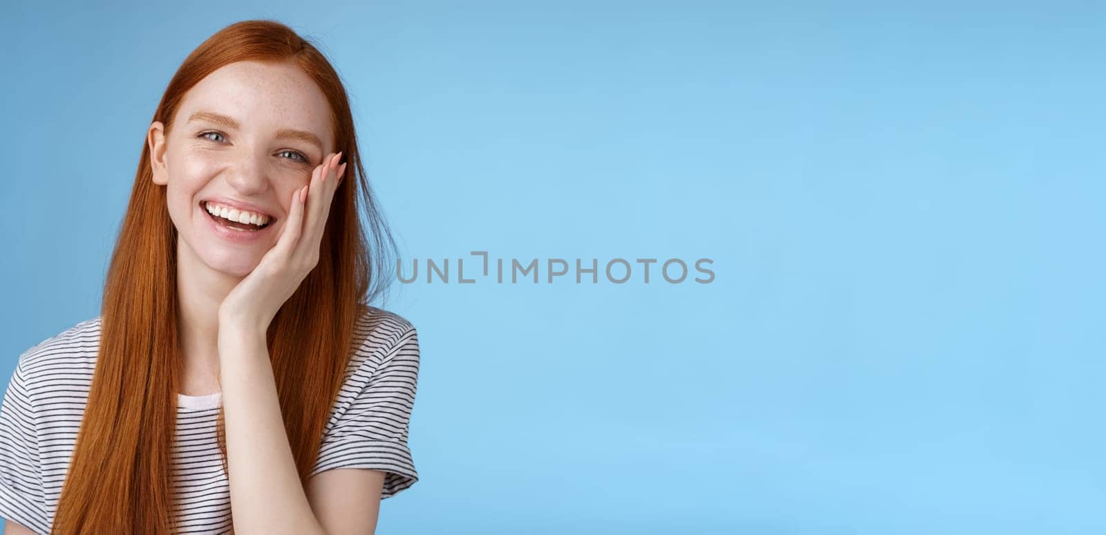 Charismatic talkative friendly-looking happy laughing redhead girl having fun discuss previous summer holidays make jokes chuckling touching face amused standing cheerful blue background by Benzoix