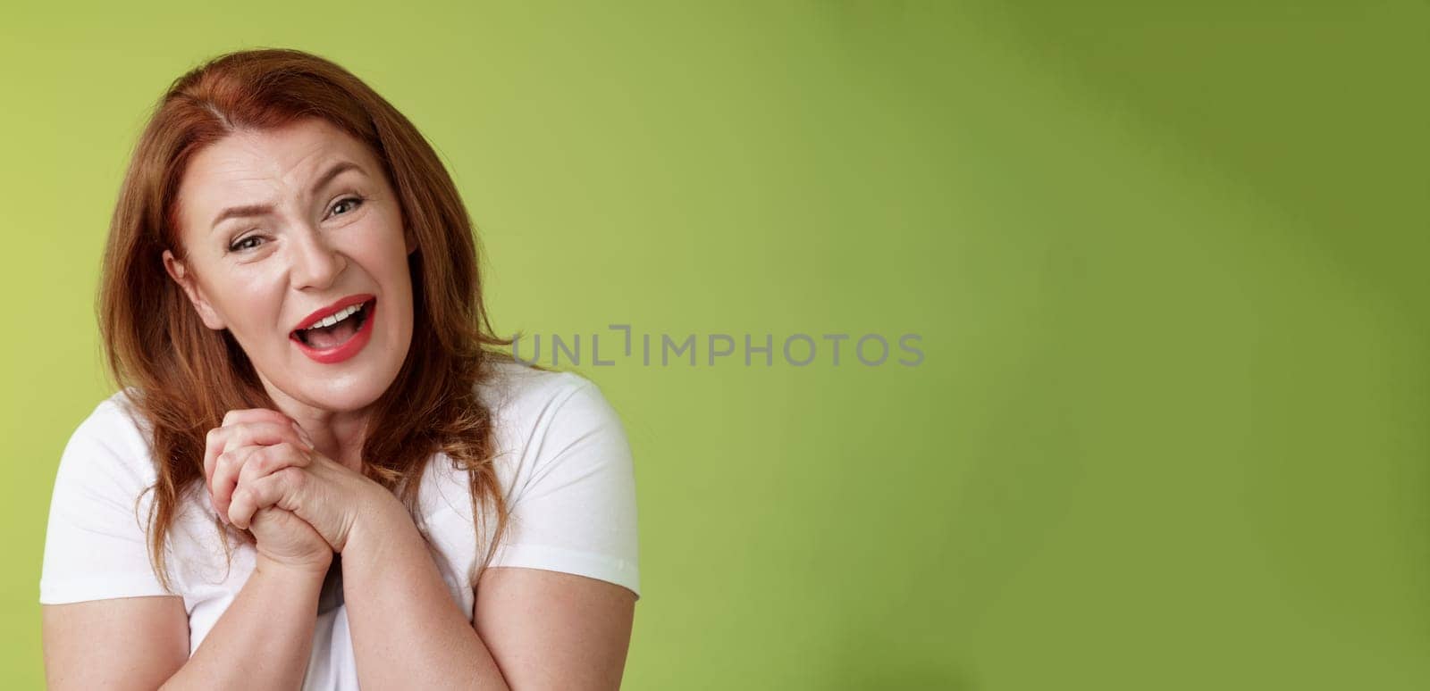 Close-yp touched tender kind redhead middle-aged granny. sighing look admiration delight clasp hands heartwarming lovely scene smiling tilting head impressed satisfied stand green background.