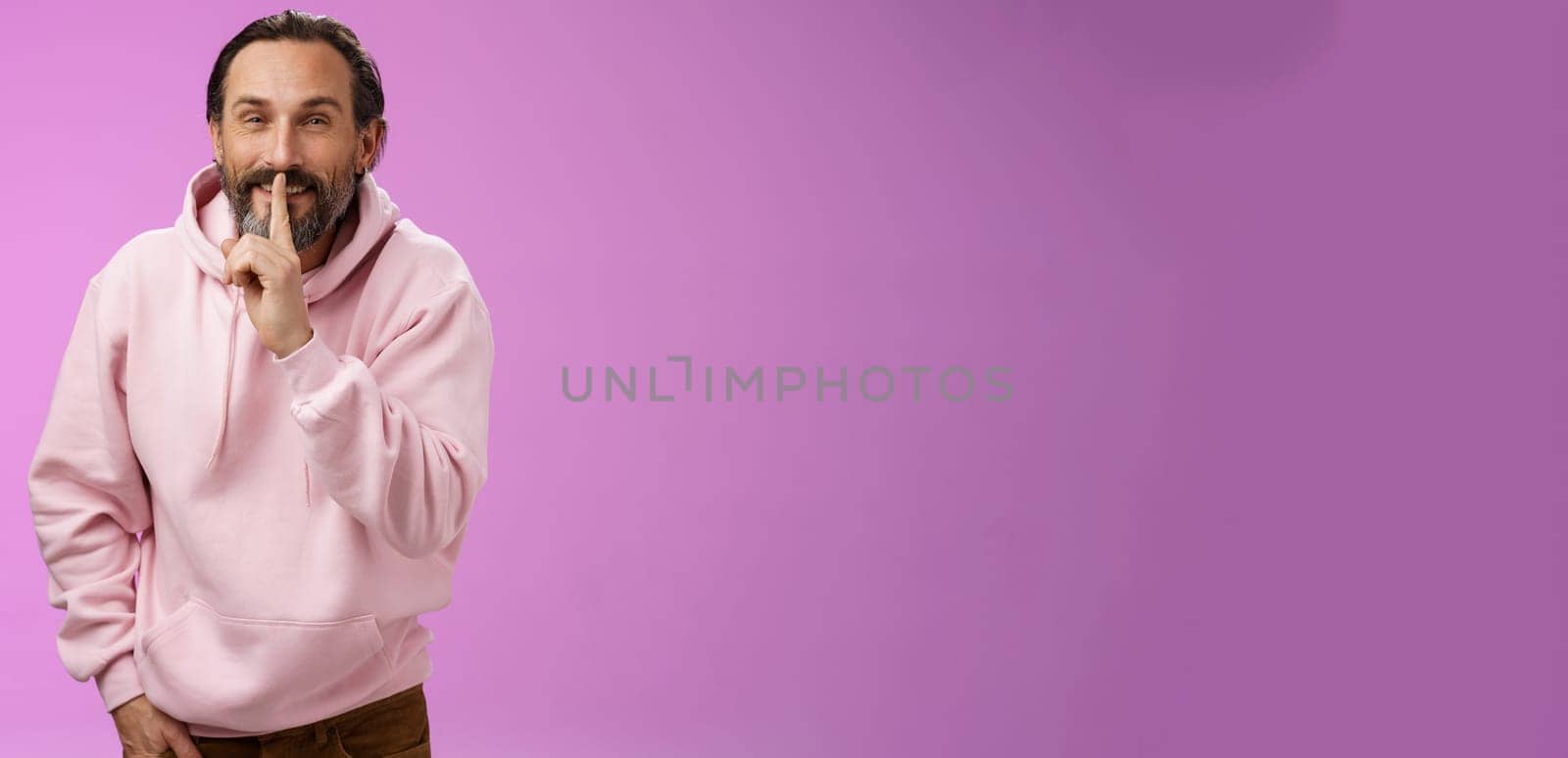 Lips sealed secret. Portrait alluring cheeky stylish adult bearded guy in pink hoodie asking keep quiet show shush shh gesture index finger pressed mouth smiling devious smug face, have idea by Benzoix