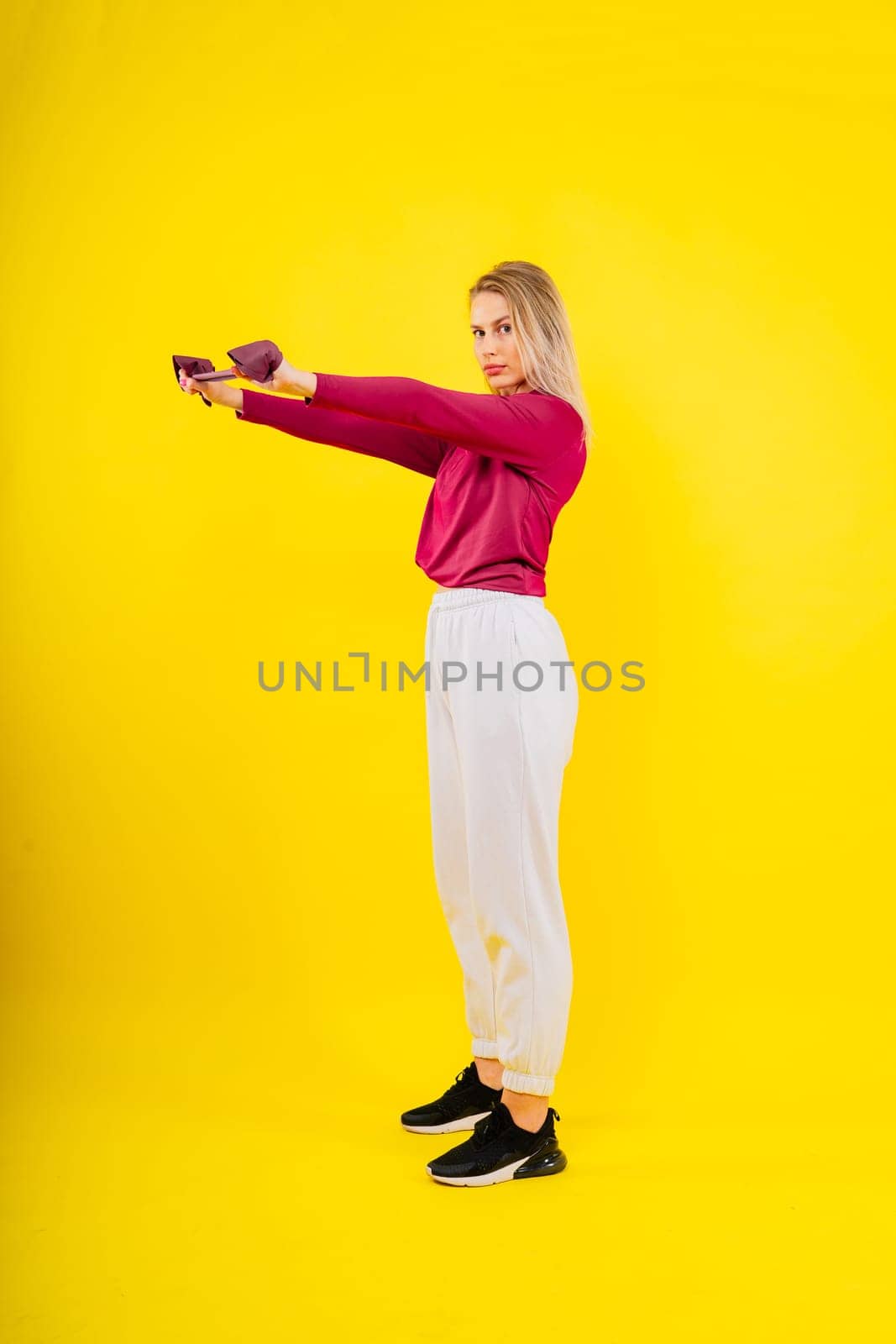 Sports woman in fashion sportswear exercising with elastic band in studio by Zelenin