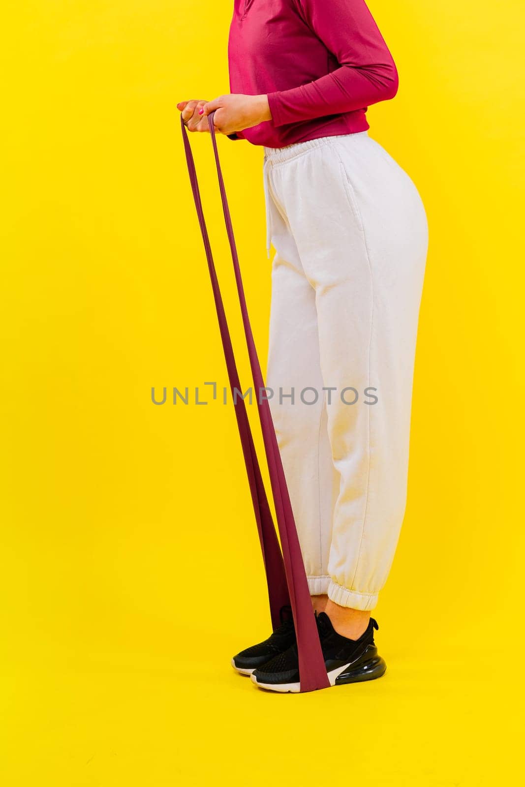 Sports woman in fashion sportswear exercising with elastic band in studio by Zelenin