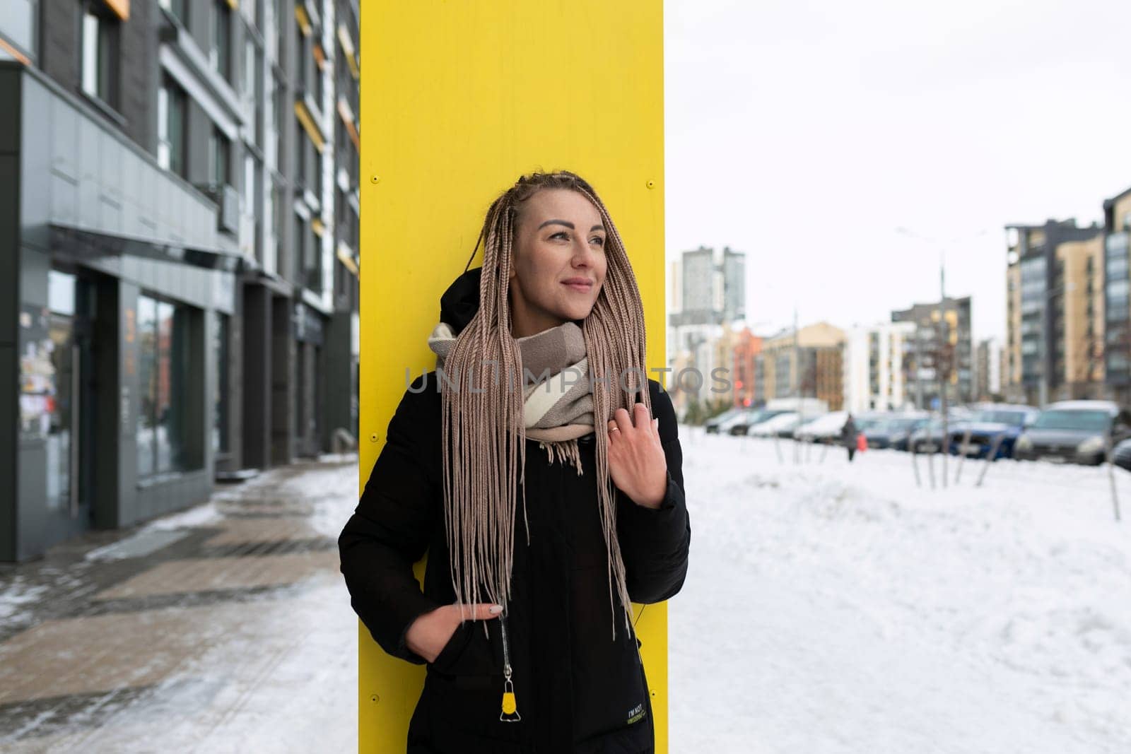 A well-groomed young woman with blond dreadlocks walks down the street in the cold.