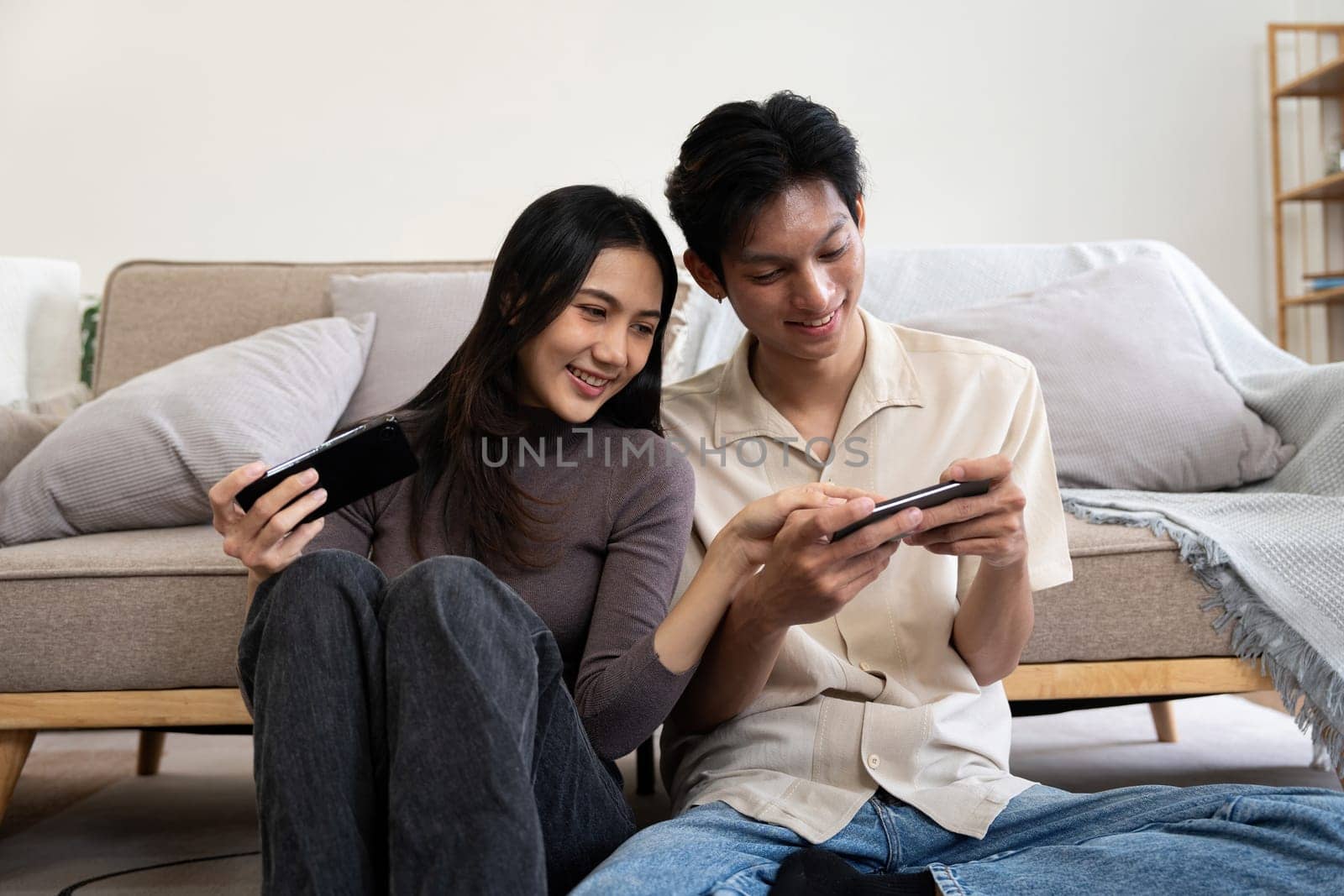 Happy couple asian young women happy enjoy playing match game online game happy relax smile laugh joy fun video gaming app. on couch in living room at home by nateemee