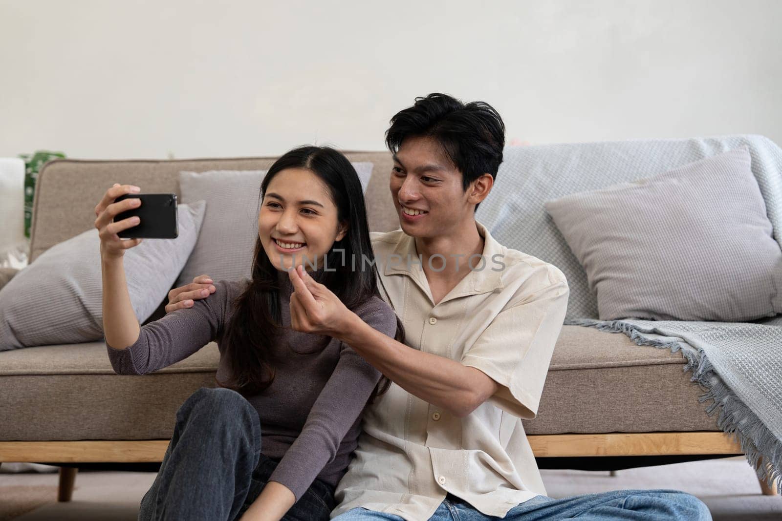 Happy couple asian young women happy smile and taking selfie on couch in living room at home by nateemee
