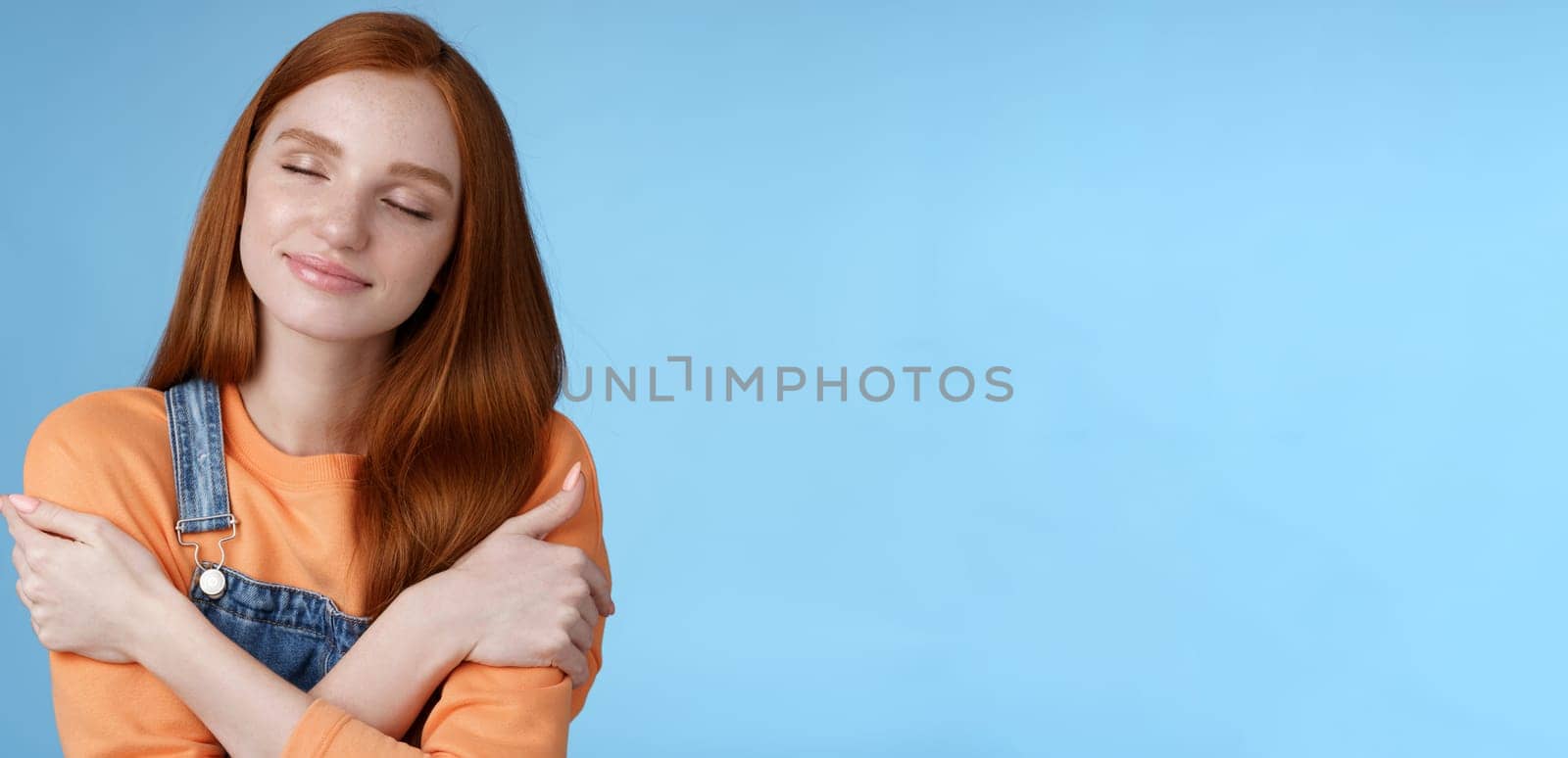Passionate romantic tender ginger girl feel safe comfort close eyes smiling gently lovely daydreaming hugging herself recalling boyfriend cuddles sensual embraces, standing blue background happy by Benzoix
