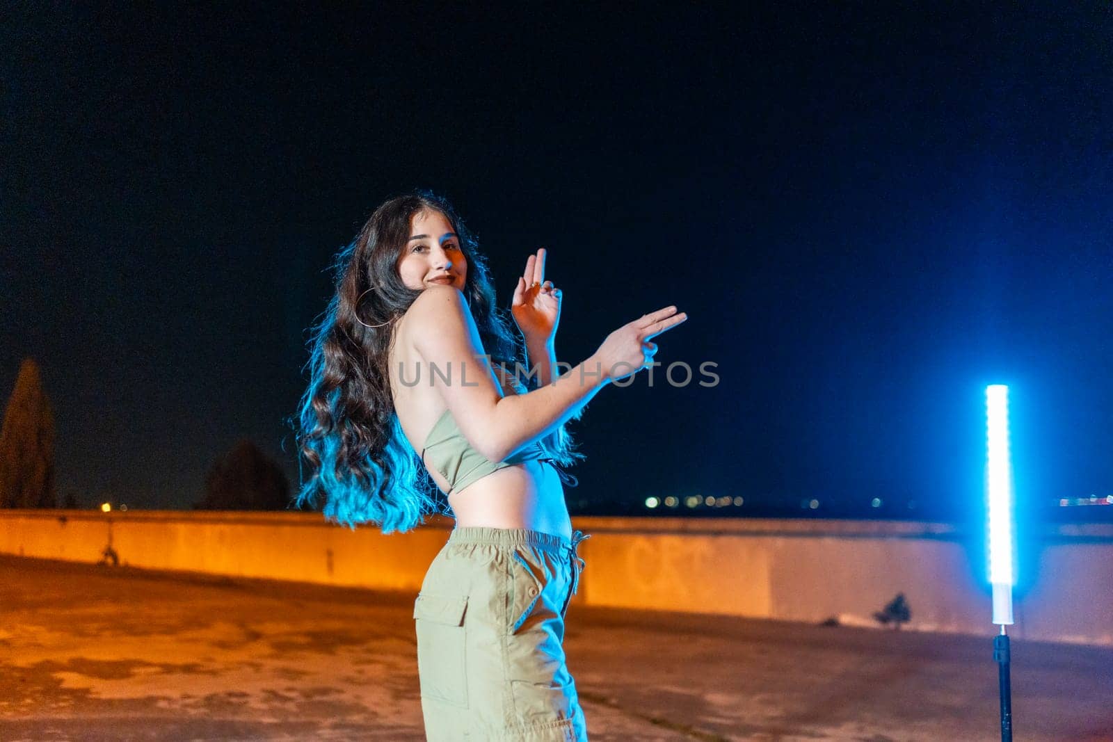Happy woman dance freestyle hip hop music in the street at night surrounded by neon lights