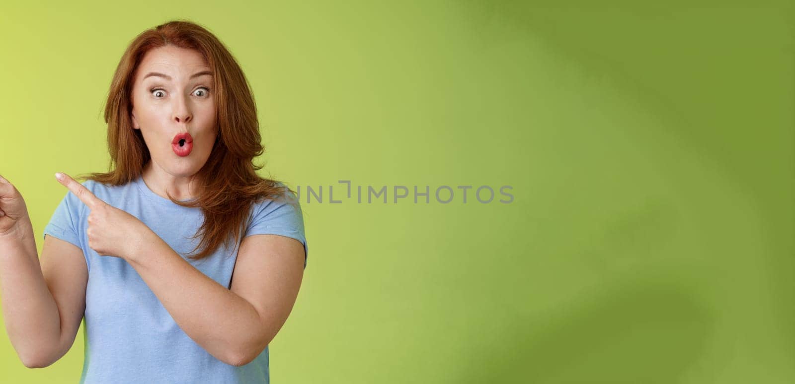 Surprised fascinated enthusiastic redhead middle-aged woman impressed awesome promo fold lips curiousity admiration stare camera thrilled pointing upper left corner great sale advertisement.