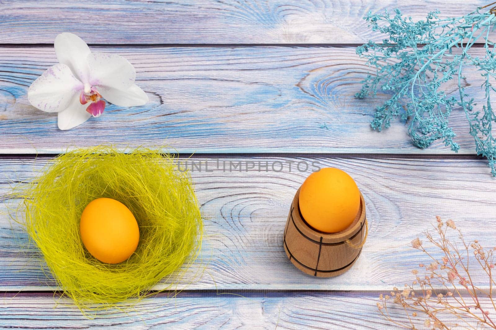 Nest with Easter egg, a small wooden barrel with an egg and an orchid flower on the boards with decorative plants. Top view.