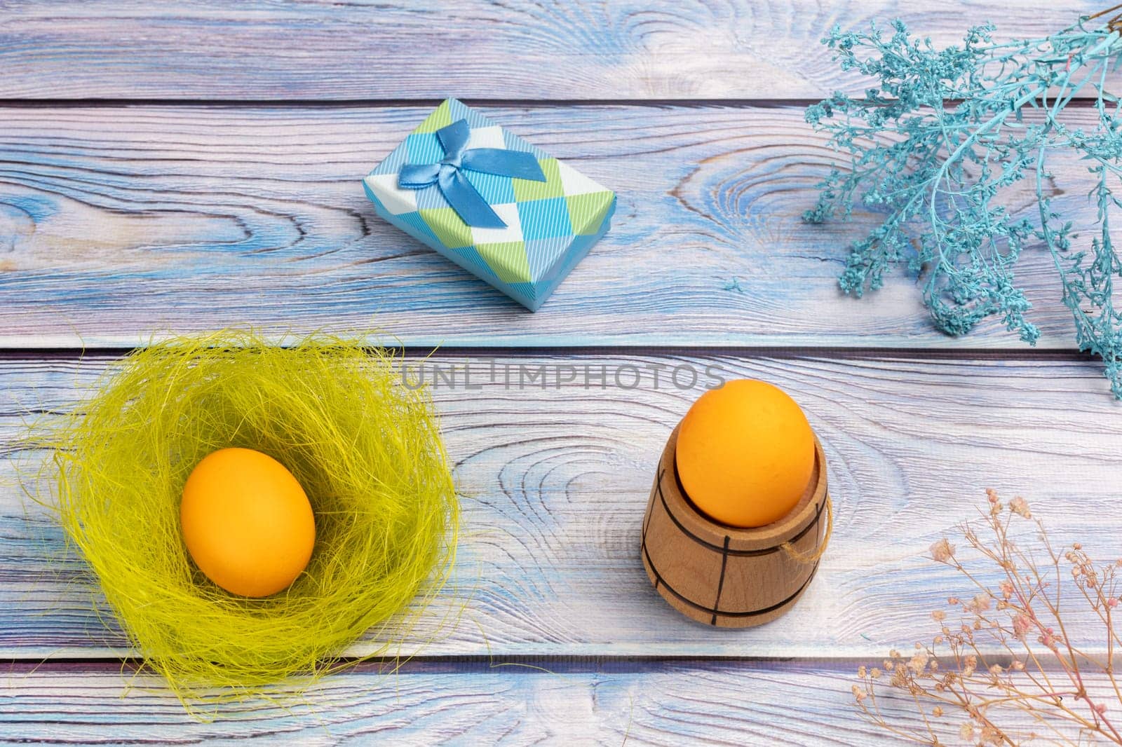 Nest with Easter egg, a gift box and a small wooden barrel with an egg on the boards with decorative plants. Top view.