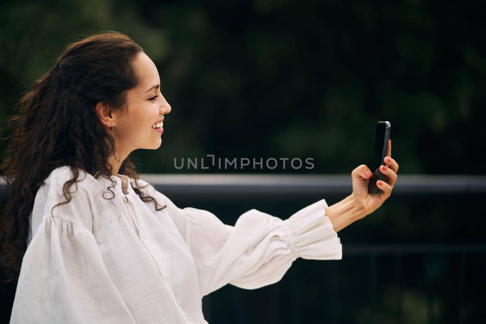 Profile of a curly brunette girl taking a selfie in the park. High quality photo