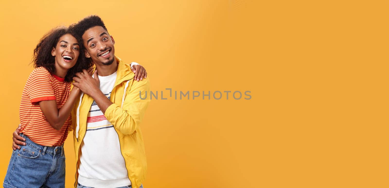 Friends always cover each other. Stylish and carefree loving african american girlfriend hugging boyfriend and smiling broadly touching guy palm hanging around and spending time great together.