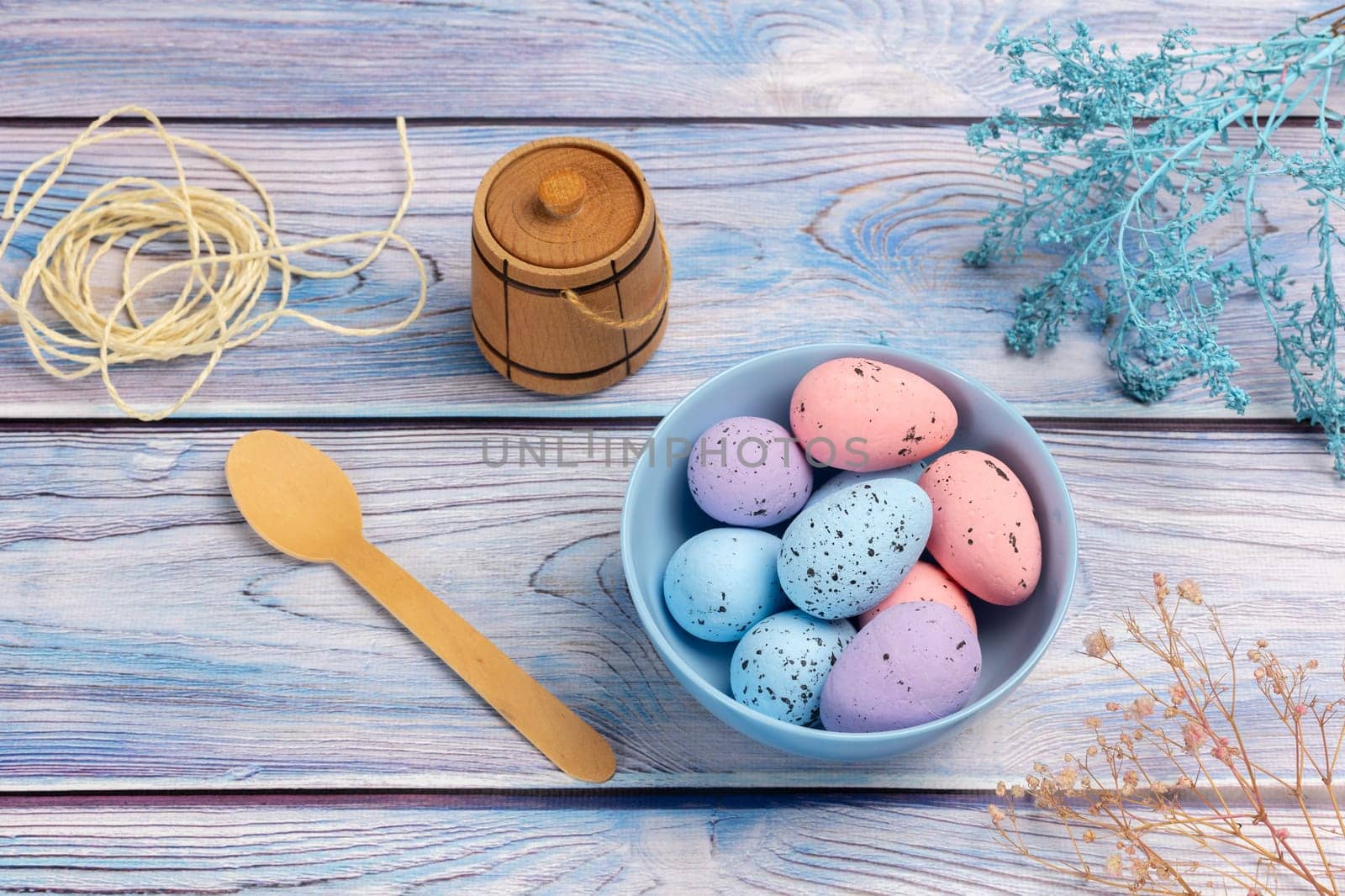 Bowl with colored Easter eggs, a small wooden barrel, a wooden spoon and a rope on the boards. Top view.