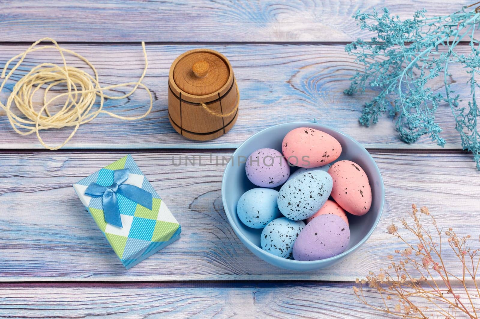 Bowl with colored Easter eggs, a gift box, a small wooden barrel and a rope on the boards. Top view.