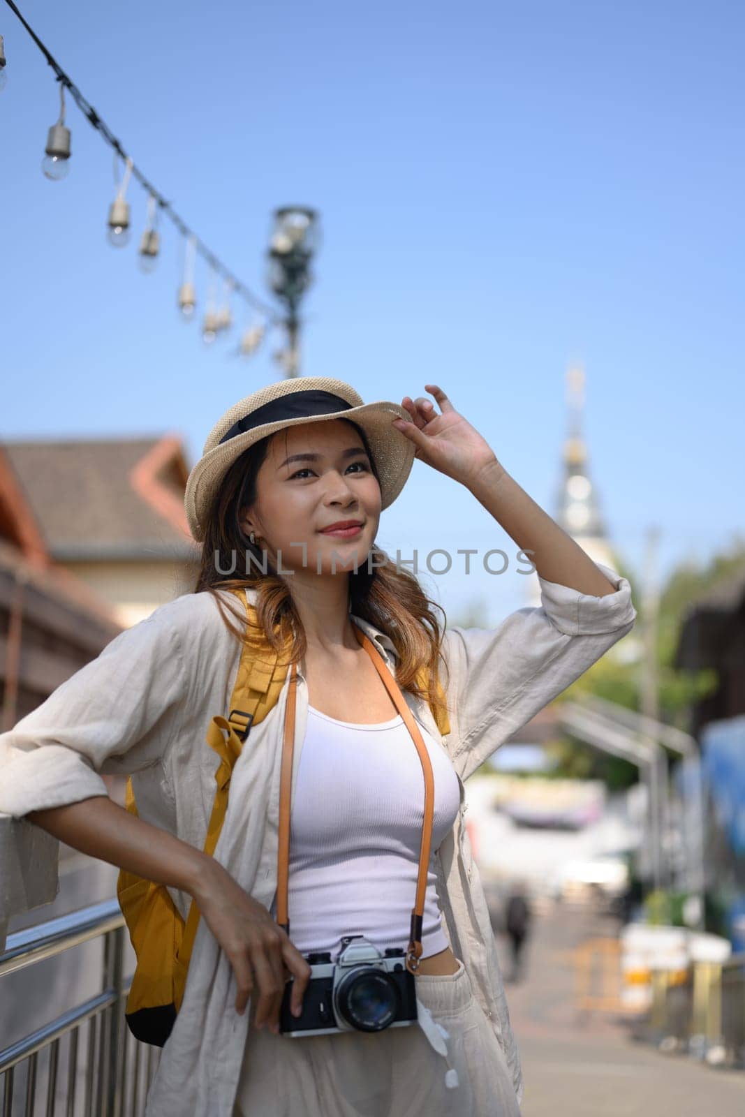 Happy young adult female tourist with backpack standing on bridge in a local city by prathanchorruangsak