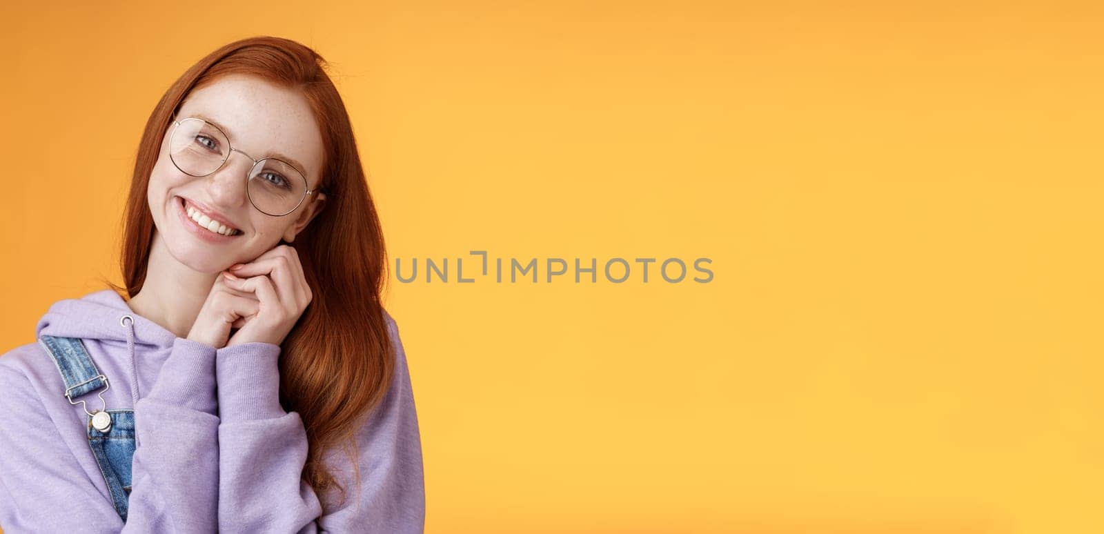 Tender feminine ginger girl blue eyes wearing glasses hoodie lean palms smiling receive sweet cute gift think you lovely grateful dearest friend grinning joyful spread love, orange background.