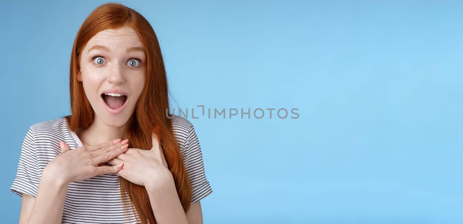Amused happy grateful european redhead woman gasping drop jaw joyfully press palms chest thankful staring surprised incredible cool gift receive awesome proposal standing blue background.