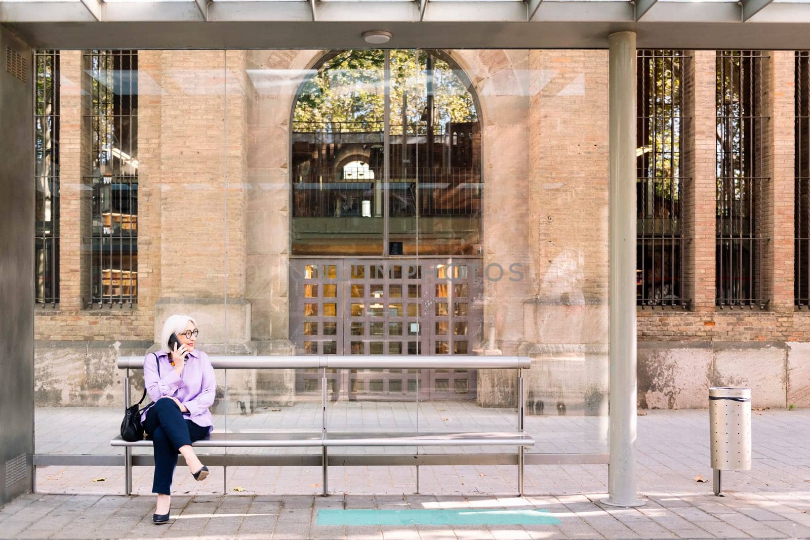 senior woman waiting at bus stop talking on phone by raulmelldo