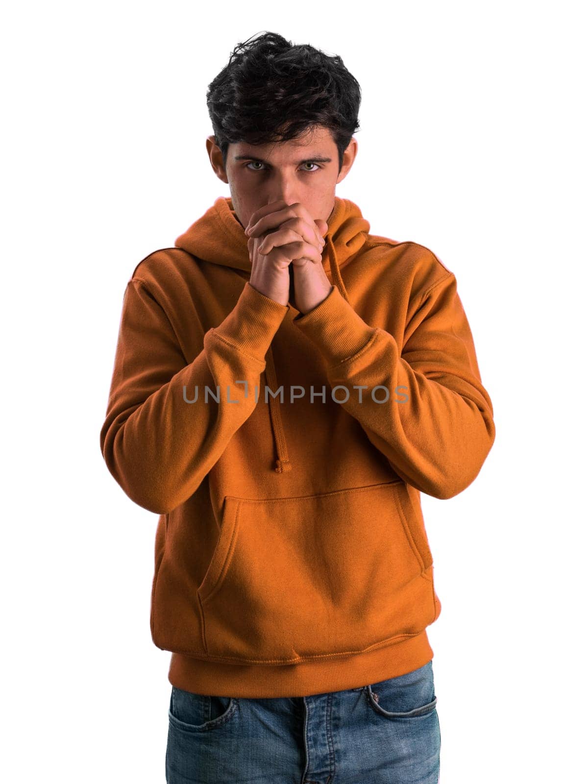 A man wearing an orange hoodie is standing with his hands clasped together. He appears thoughtful and contemplative as he stands in a casual pose.