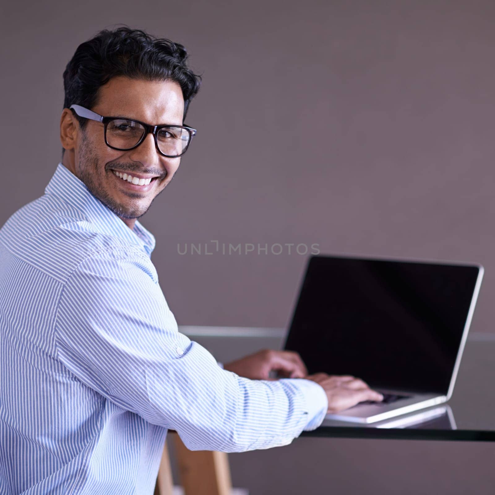 Indian businessman, smile and portrait on laptop, technology and screen in office. Happiness, eyewear and computer for entrepreneur working on project, typing and keyboard for notes and research by YuriArcurs