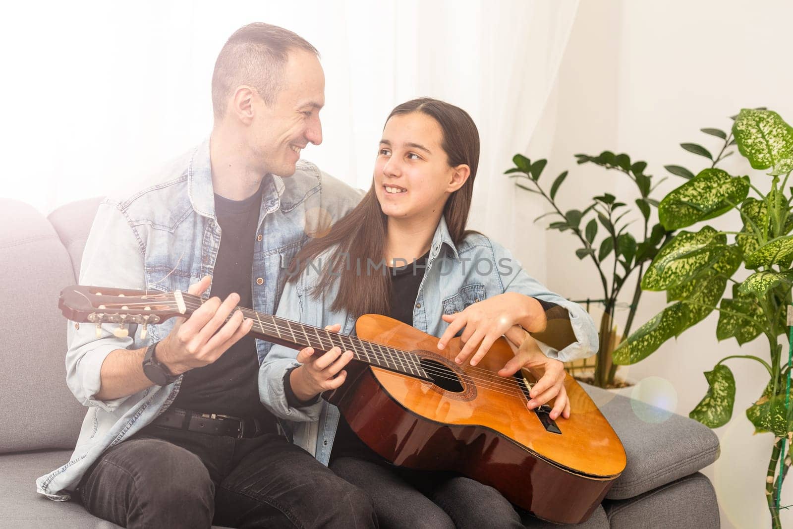 smiling father showing daughter how to play barre chord by Andelov13