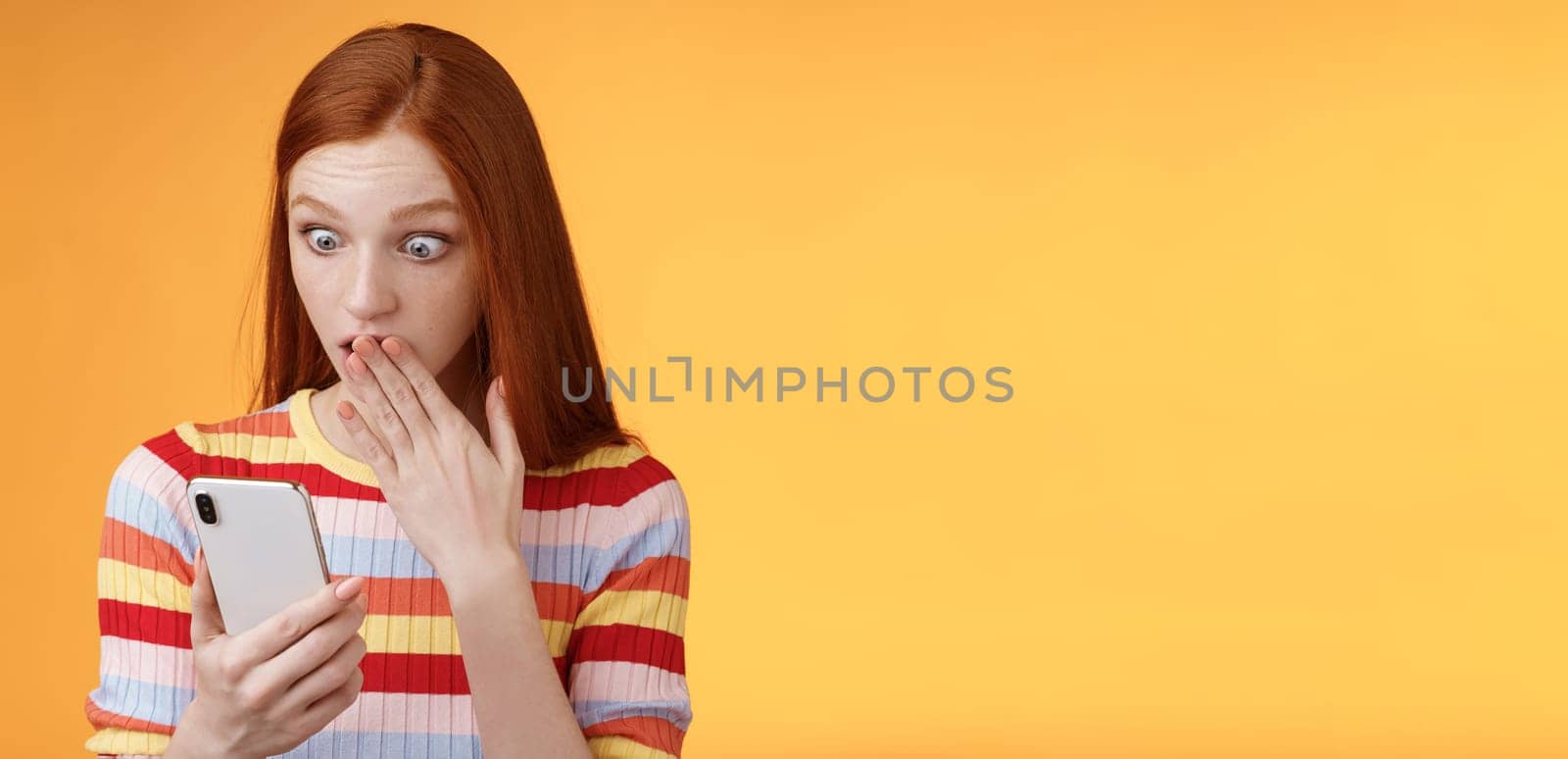 Woman receive shocking message gasping cover mouth palm staring smartphone display found out who follow boyfriend internet social network standing amazed thrilled, orange background.