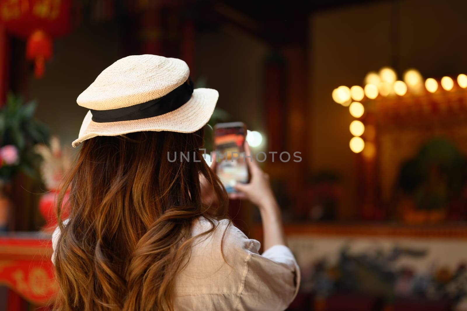 Back view of young woman taking photo of Chinese temple with mobile phone by prathanchorruangsak