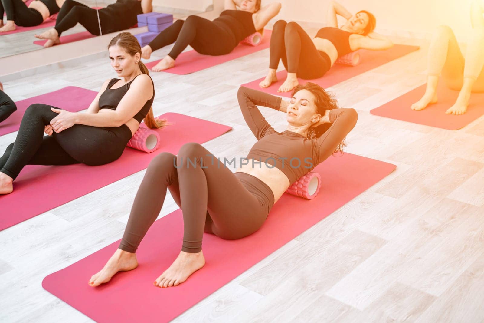 Athletic women doing fascia exercises on the floor with a foam roller massage tool to relieve back tension and relieve muscle pain. The concept of physiotherapy and stretching training by Matiunina