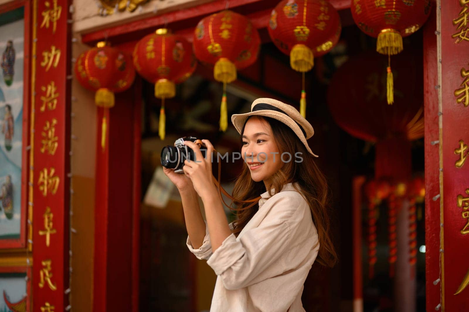 Smiling young woman standing at Chinese Temple with beautiful red lanterns adorning, taking photo with camera by prathanchorruangsak