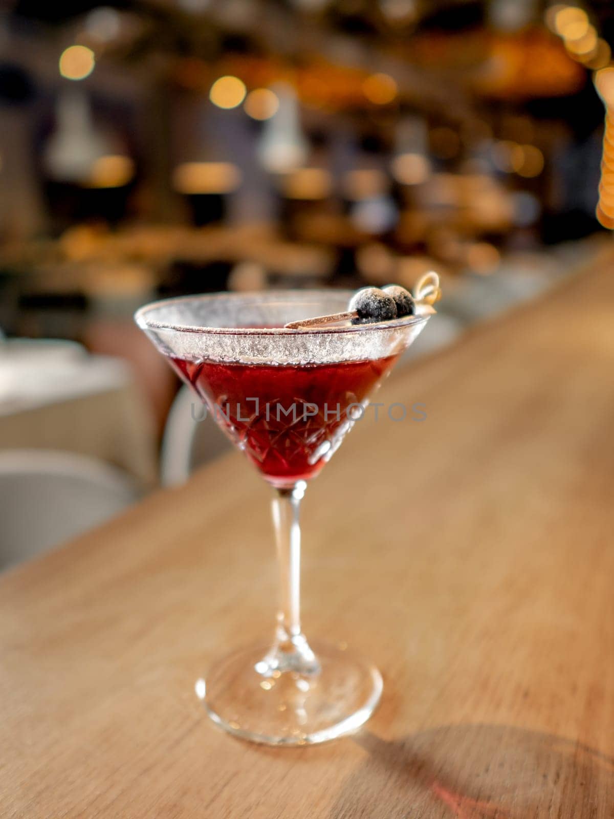 Red cocktail in martini glass on bar counter. Cranberry or blackberry and gin alcohol cocktail decorated white powdered sugar and black olive. Decorate cold alcoholic cocktail with sugar powder in bar