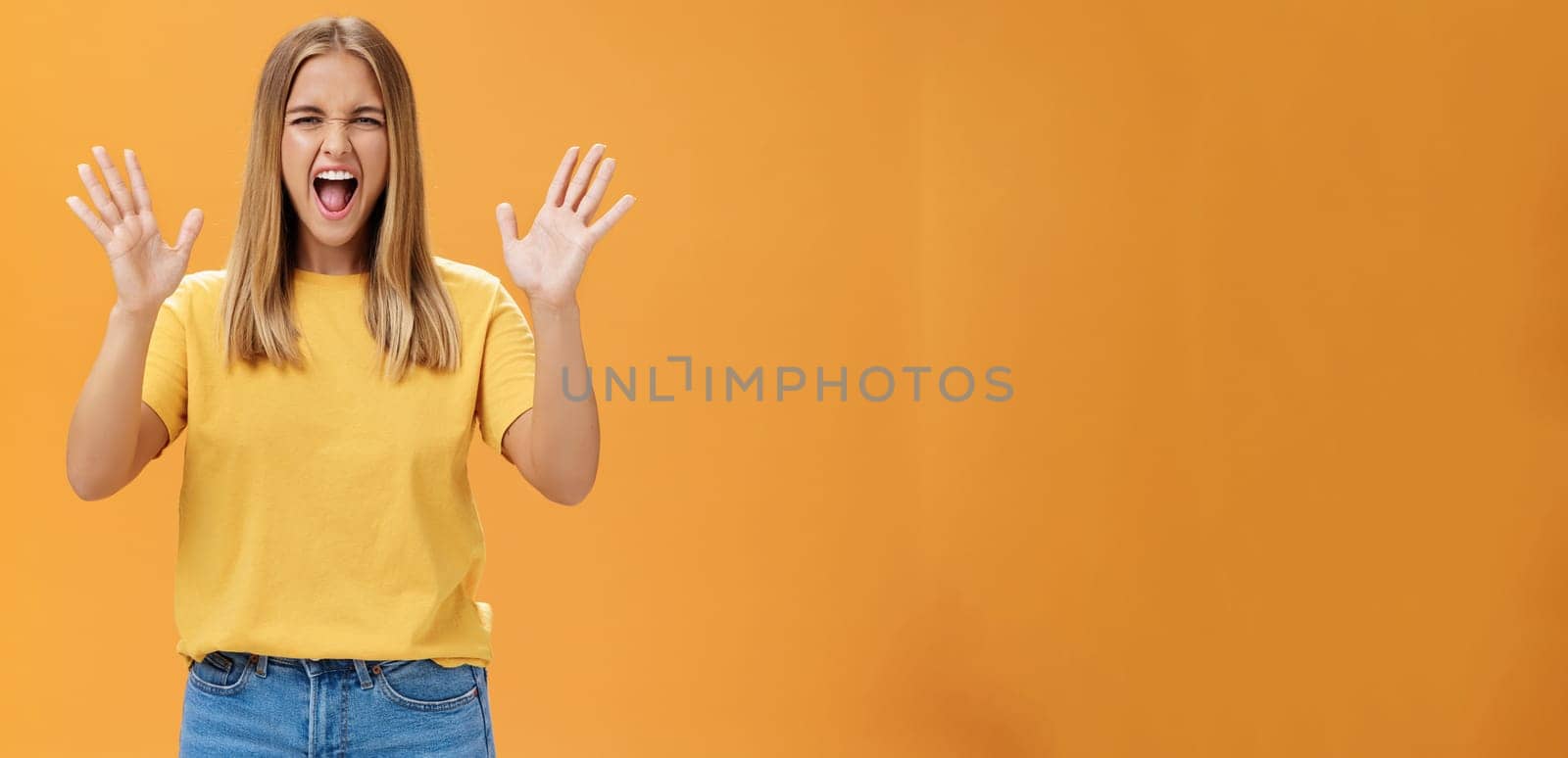 Woman releasing stress yelling with joy and pleasure gesturing with raised arms being daring and rebellious not afraid to show emotions standing passionate and expressive against orange background. Body language concept