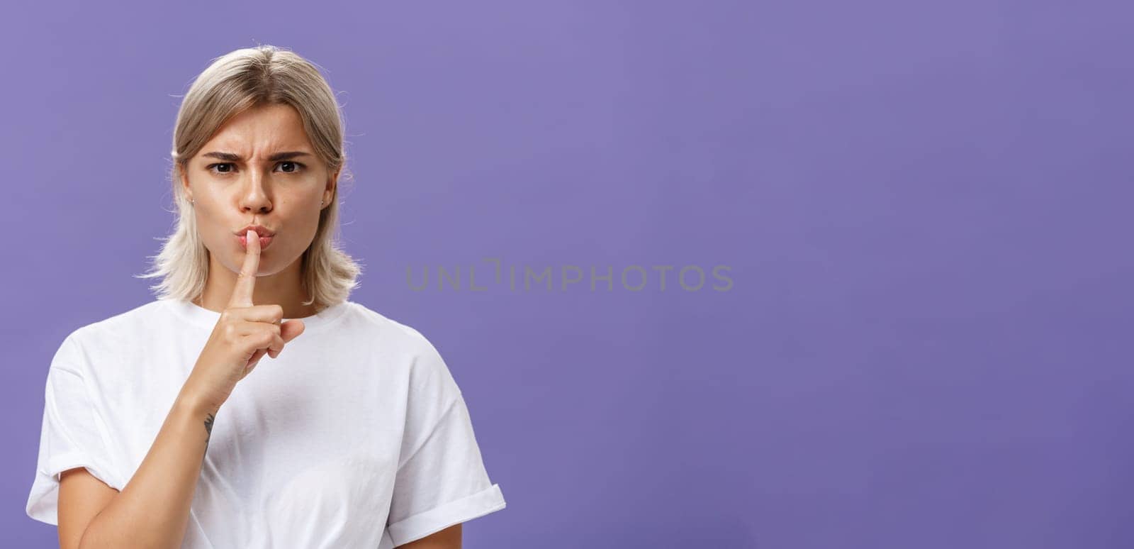 Lifestyle. Close-up shot of serious strict good-looking caucasian female with blond hair shushing at camera displeased and disappointed frowning holding index finger over folded lips in shush sign.