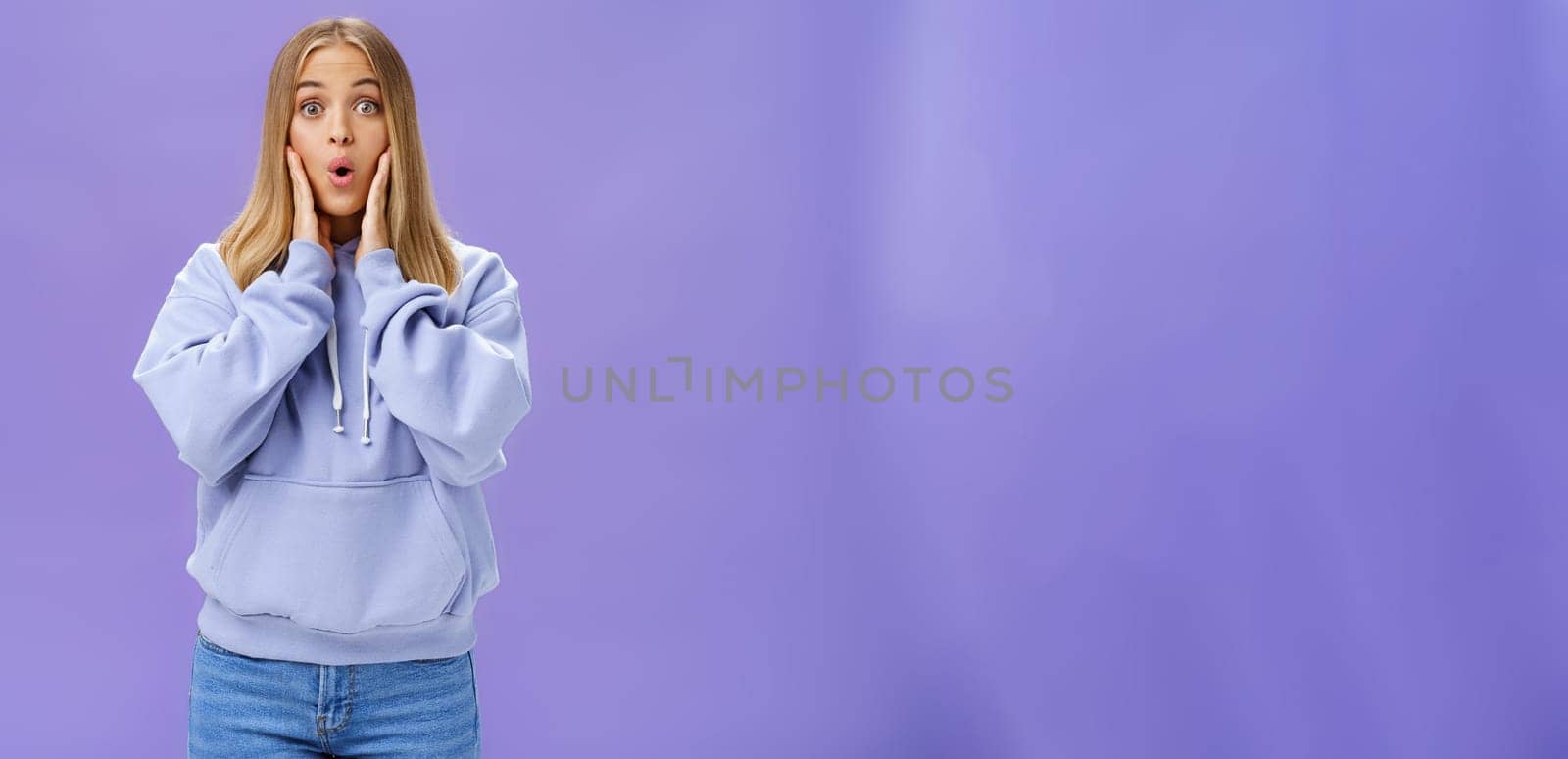 Indoor shot of amused and thrilled surprised good-looking young woman in stylish hoodie folding lips in wow sound popping eyes at camera shocked and excited learning amazing news over purple wall by Benzoix