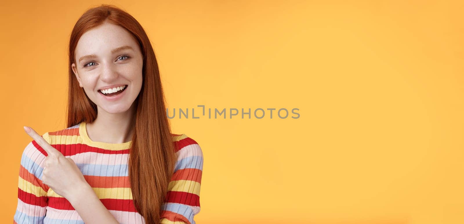 Friendly outgoing good-looking ginger girl university student discussing lecture classmate smiling laughing pointing upper left corner questioned curious know details standing orange background by Benzoix