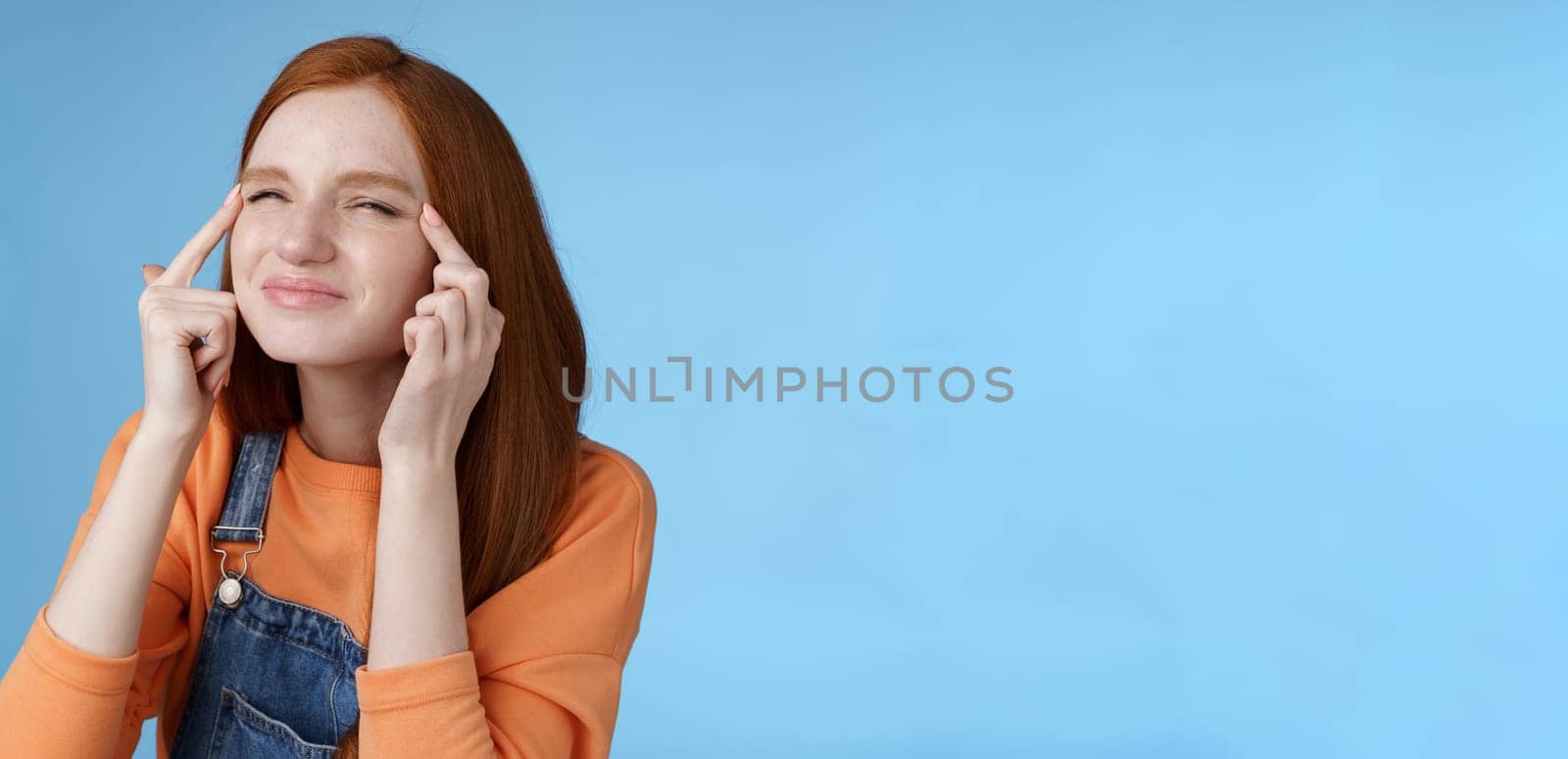 Cute funny european redhead girl forgot glasses trying read sigh stretch eyelids squinting frowning focused look upper left corner perplexed see what happening, standing blue background by Benzoix