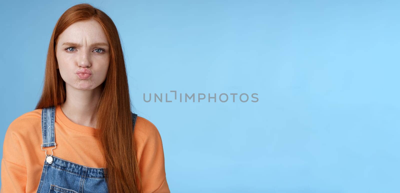 Moody displeased clingy girlfriend redhead blue eyes pouting sulking upset offended frowning making grimace showing attitude standing disappointed unsatisfied blue background, complaining by Benzoix